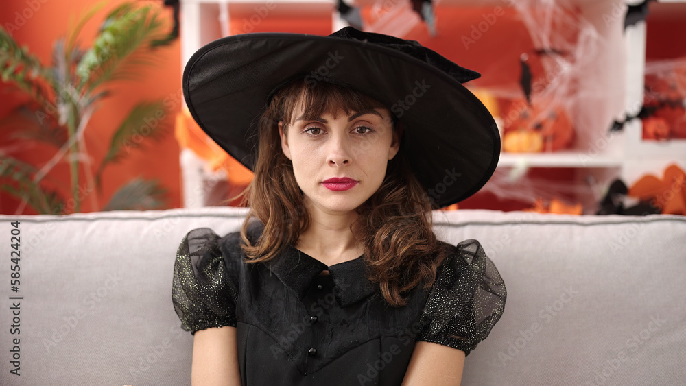 Young caucasian woman looking serious wearing witch costume sitting on the sofa at home Young caucasian woman looking serious wearing witch costume sitting on the sofa at home