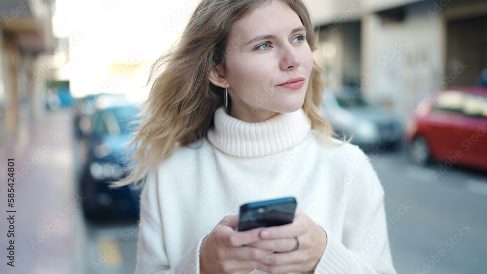 Fototapeta premium Young blonde woman using smartphone standing at street