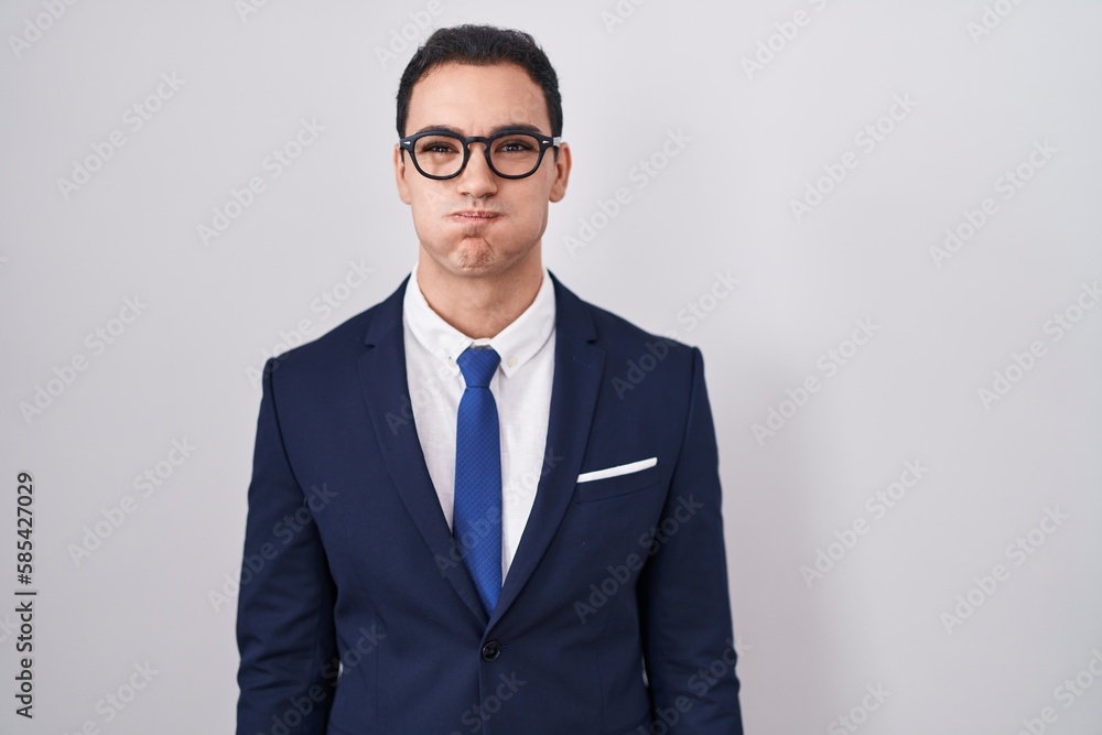 Young hispanic man wearing suit and tie puffing cheeks with funny face. mouth inflated with air, crazy expression. Young hispanic man wearing suit and tie puffing cheeks with funny face. mouth inflated with air, crazy expression.