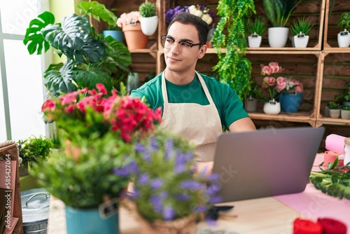 Young hispanic man florist smiling confident using laptop at flower shop © Krakenimages.com