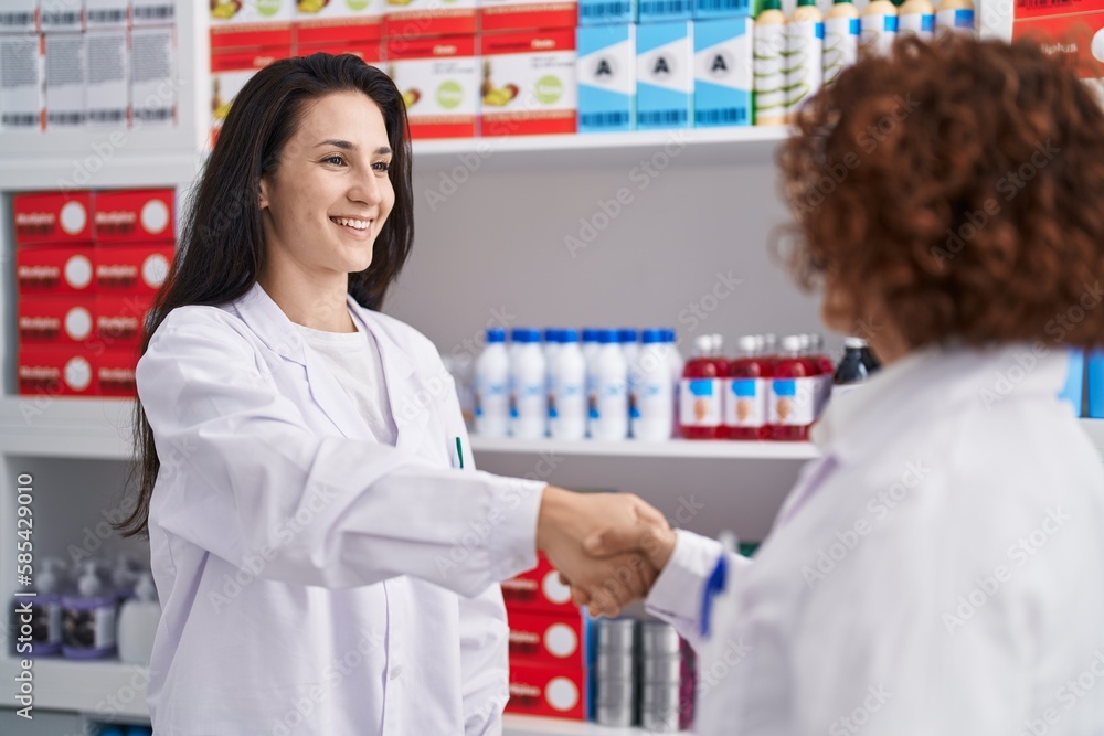 Two women pharmacists smiling confident shake hands at pharmacy