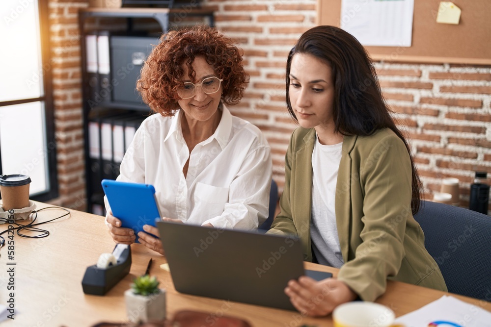 Two women business workers using laptop and touchpad working at office Two women business workers using laptop and touchpad working at office