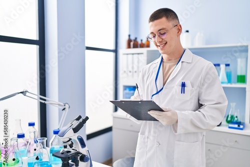 Young hispanic man scientist writing report working at laboratory