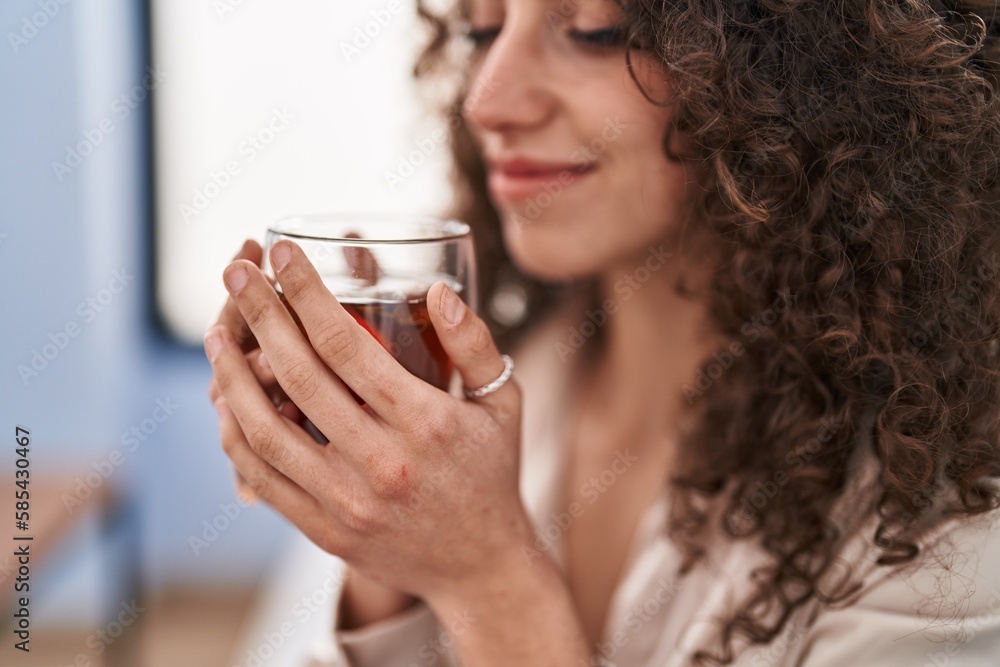 Young hispanic woman smelling tea sitting on sofa at home Young hispanic woman smelling tea sitting on sofa at home