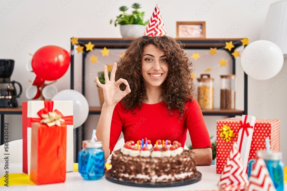 Hispanic woman with curly hair celebrating birthday holding big chocolate cake doing ok sign with fingers, smiling friendly gesturing excellent symbol Hispanic woman with curly hair celebrating birthday holding big chocolate cake doing ok sign with fingers, smiling friendly gesturing excellent symbol