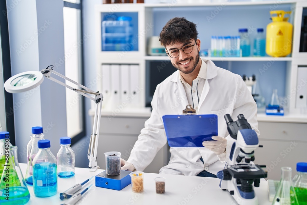 Young hispanic man scientist weighing sample reading document at laboratory Young hispanic man scientist weighing sample reading document at laboratory