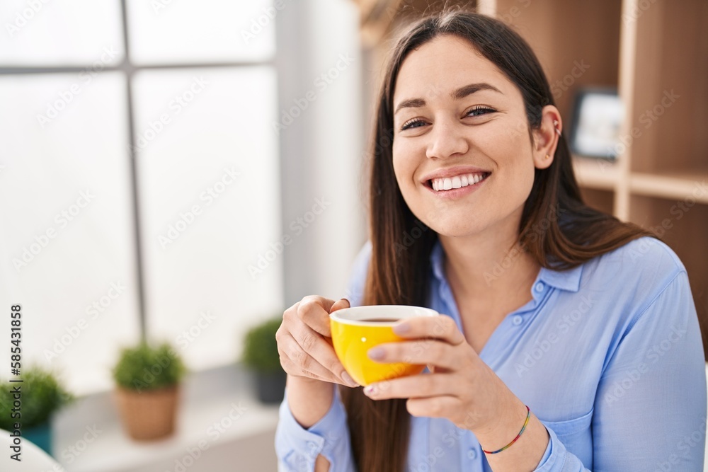 Young woman drinking coffee sitting on table at home Young woman drinking coffee sitting on table at home