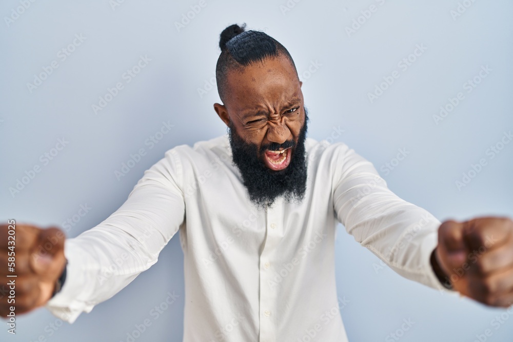 African american man standing over blue background angry and mad raising fists frustrated and furious while shouting with anger. rage and aggressive concept. African american man standing over blue background angry and mad raising fists frustrated and furious while shouting with anger. rage and aggressive concept.