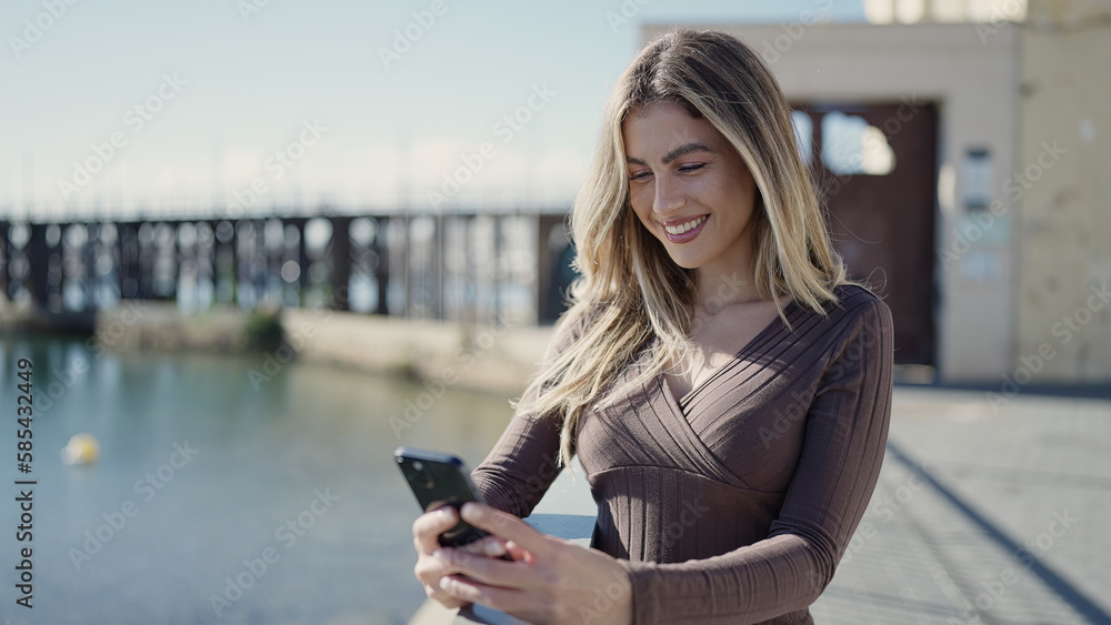 Fototapeta premium Young blonde woman smiling confident using smartphone at seaside