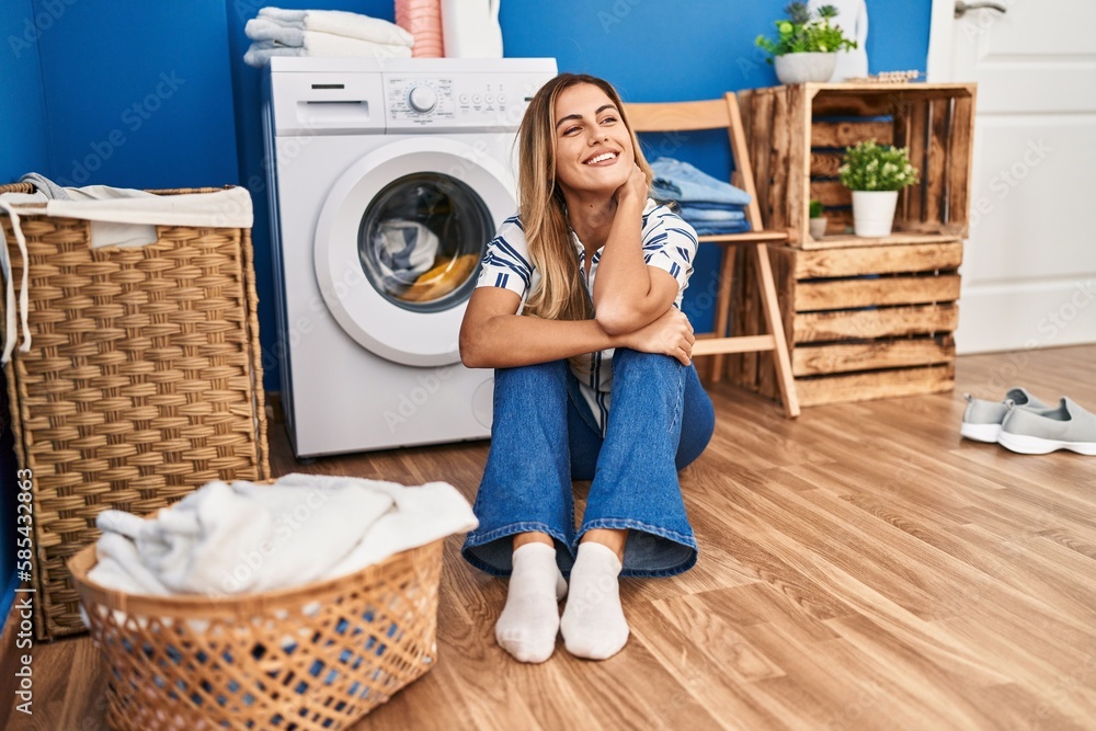 Young blonde woman sitting on the floor waiting for washing machine at laundry room Young blonde woman sitting on the floor waiting for washing machine at laundry room