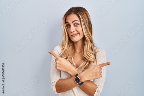 Young blonde woman standing over isolated background pointing to both sides with fingers, different direction disagree