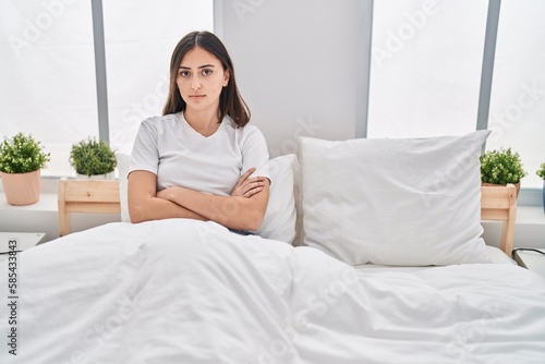 Young hispanic woman sitting on bed stressed with arms crossed gesture at bedroom