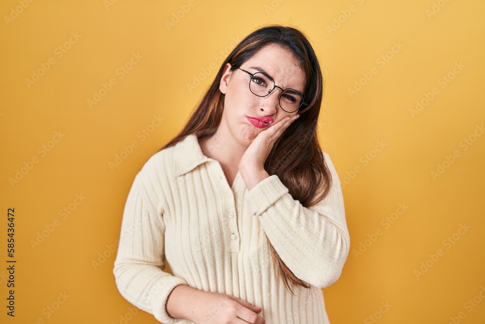 Young hispanic woman standing over yellow background thinking looking tired and bored with depression problems with crossed arms.