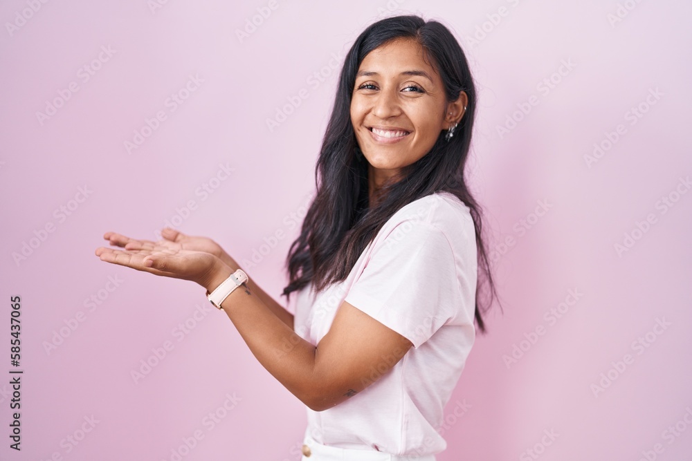 Young hispanic woman standing over pink background pointing aside with hands open palms showing copy space, presenting advertisement smiling excited happy Young hispanic woman standing over pink background pointing aside with hands open palms showing copy space, presenting advertisement smiling excited happy