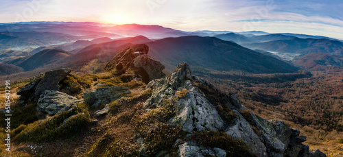 Amazing panoramic landscape of mountains range at hazy morning at sunrise. A view of the slopes of the mountains in the distance and forest hills in rays of sunlight.