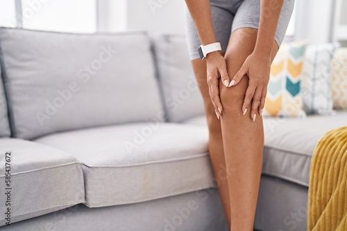 Young blonde woman touching knee for injury at home