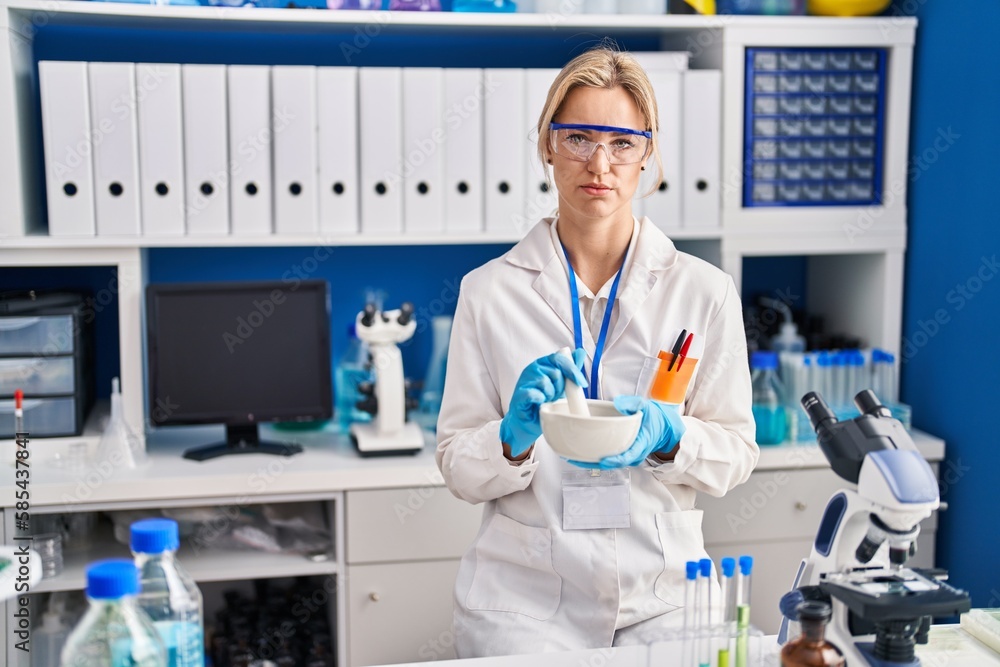 Young caucasian woman working at scientist laboratory relaxed with serious expression on face. simple and natural looking at the camera.