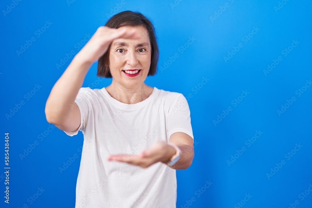 Middle age hispanic woman standing over blue background gesturing with hands showing big and large size sign, measure symbol. smiling looking at the camera. measuring concept. Middle age hispanic woman standing over blue background gesturing with hands showing big and large size sign, measure symbol. smiling looking at the camera. measuring concept.