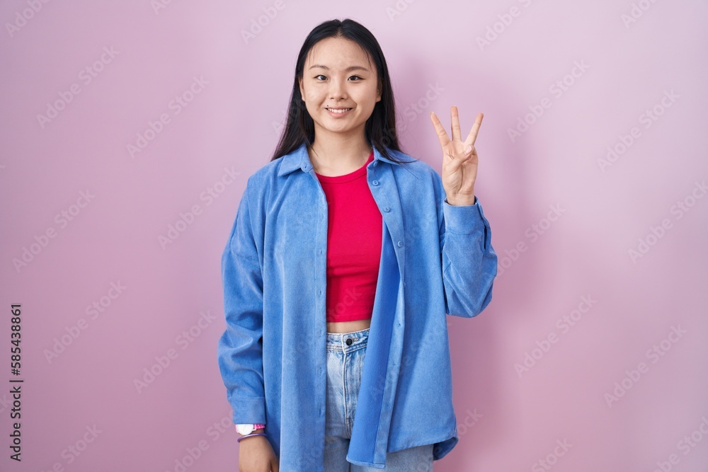 Young asian woman standing over pink background showing and pointing up with fingers number three while smiling confident and happy. Young asian woman standing over pink background showing and pointing up with fingers number three while smiling confident and happy.