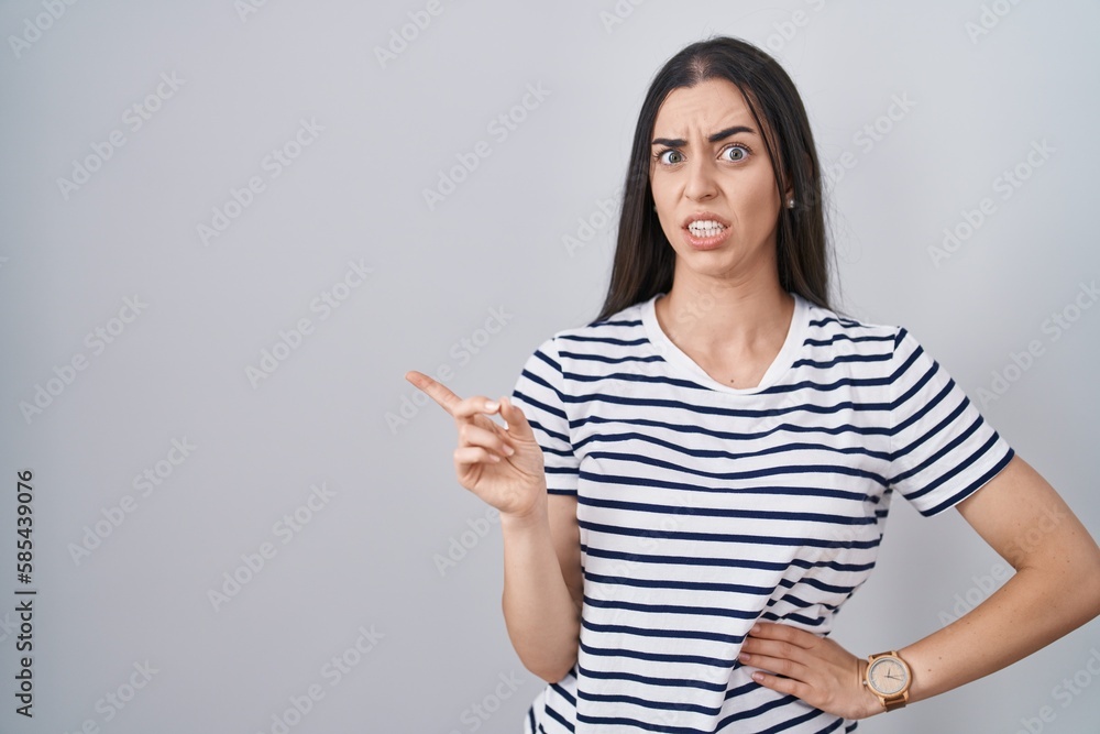 Young brunette woman wearing striped t shirt pointing aside worried and nervous with forefinger, concerned and surprised expression Young brunette woman wearing striped t shirt pointing aside worried and nervous with forefinger, concerned and surprised expression