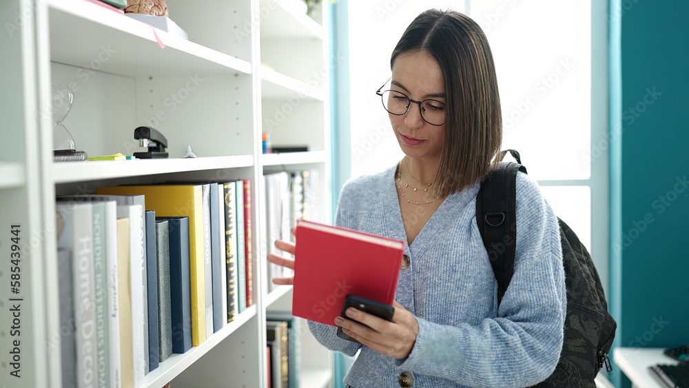 Young beautiful hispanic woman student holding book and smartphone at library university Young beautiful hispanic woman student holding book and smartphone at library university