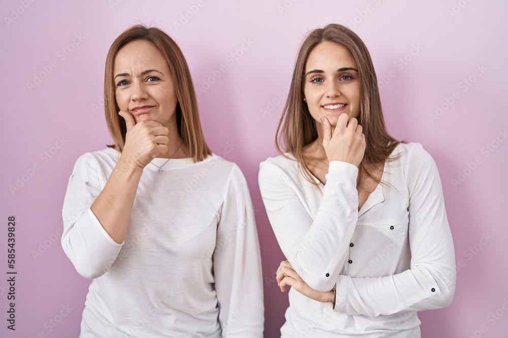 Middle age mother and young daughter standing over pink background looking confident at the camera smiling with crossed arms and hand raised on chin. thinking positive. Middle age mother and young daughter standing over pink background looking confident at the camera smiling with crossed arms and hand raised on chin. thinking positive.