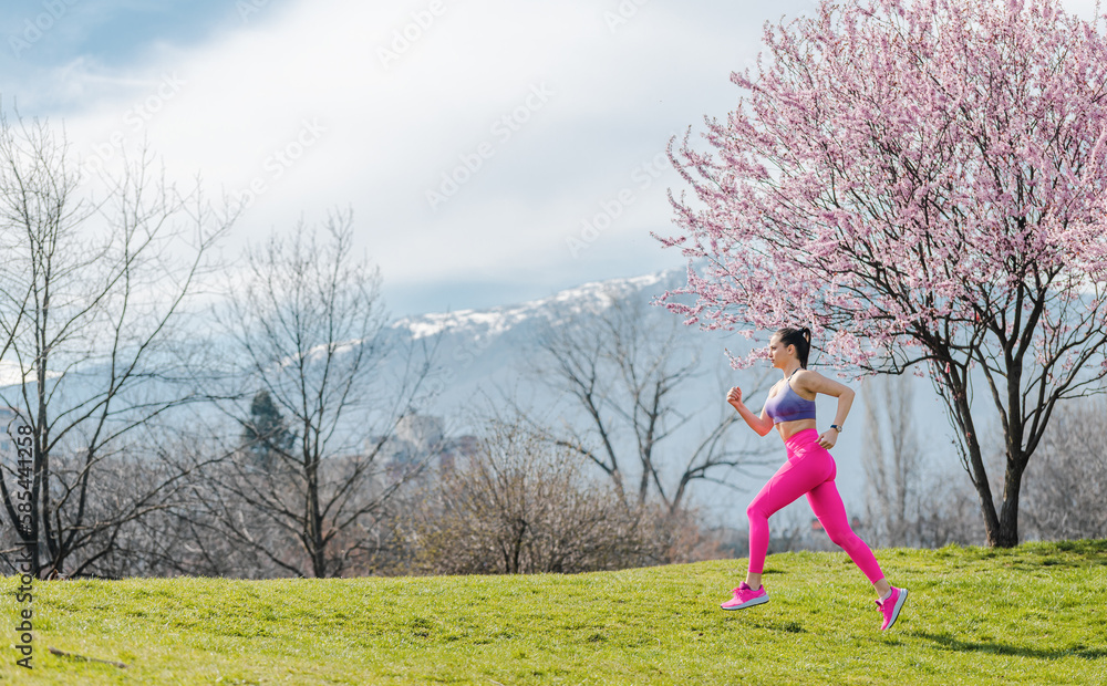 Woman doing sport running on hill between cherry trees blossoming