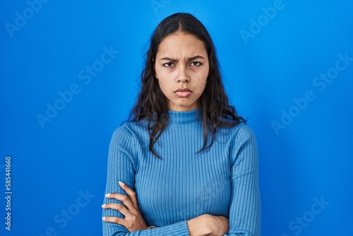 Young brazilian woman standing over blue isolated background skeptic and nervous, disapproving expression on face with crossed arms. negative person.