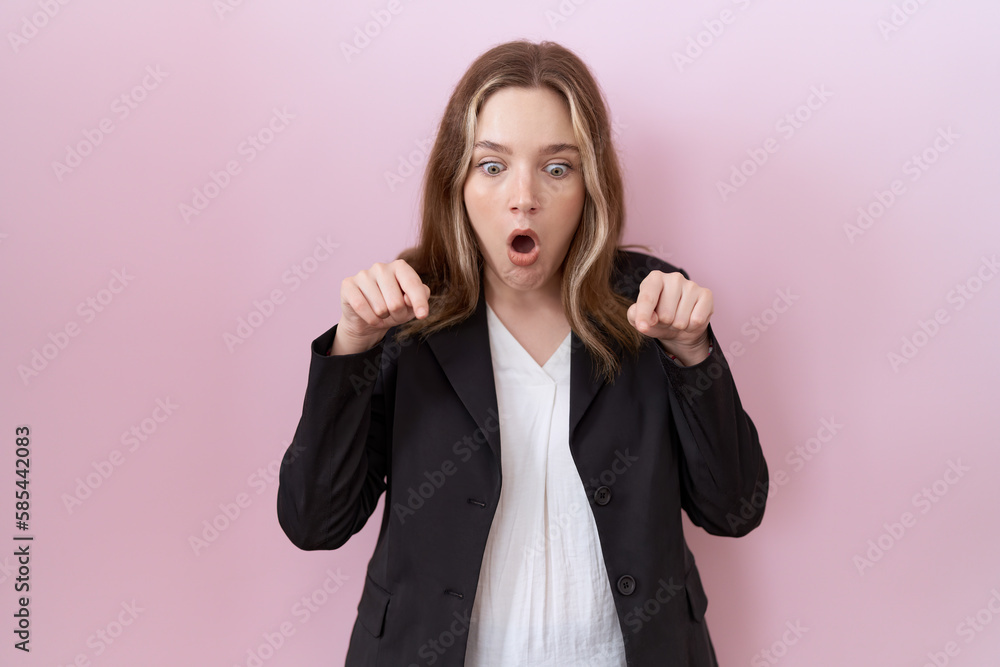 Young caucasian business woman wearing black jacket pointing down with fingers showing advertisement, surprised face and open mouth