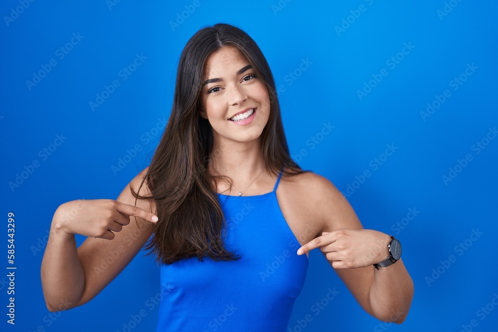 Hispanic woman standing over blue background looking confident with smile on face, pointing oneself with fingers proud and happy. Hispanic woman standing over blue background looking confident with smile on face, pointing oneself with fingers proud and happy.