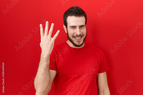 Young hispanic man wearing casual red t shirt showing and pointing up with fingers number four while smiling confident and happy. © Krakenimages.com
