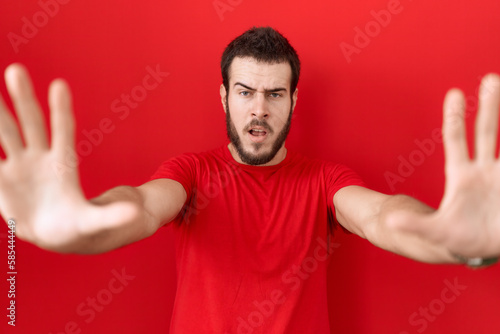 Young hispanic man wearing casual red t shirt doing stop gesture with hands palms, angry and frustration expression © Krakenimages.com