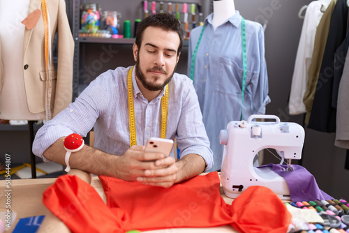 Young hispanic man tailor smiling confident using smartphone at atelier