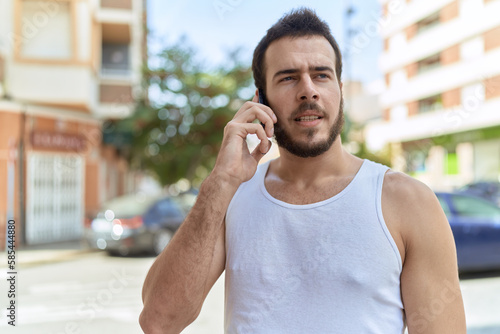 Young hispanic man talking on smartphone with relaxed expression at street