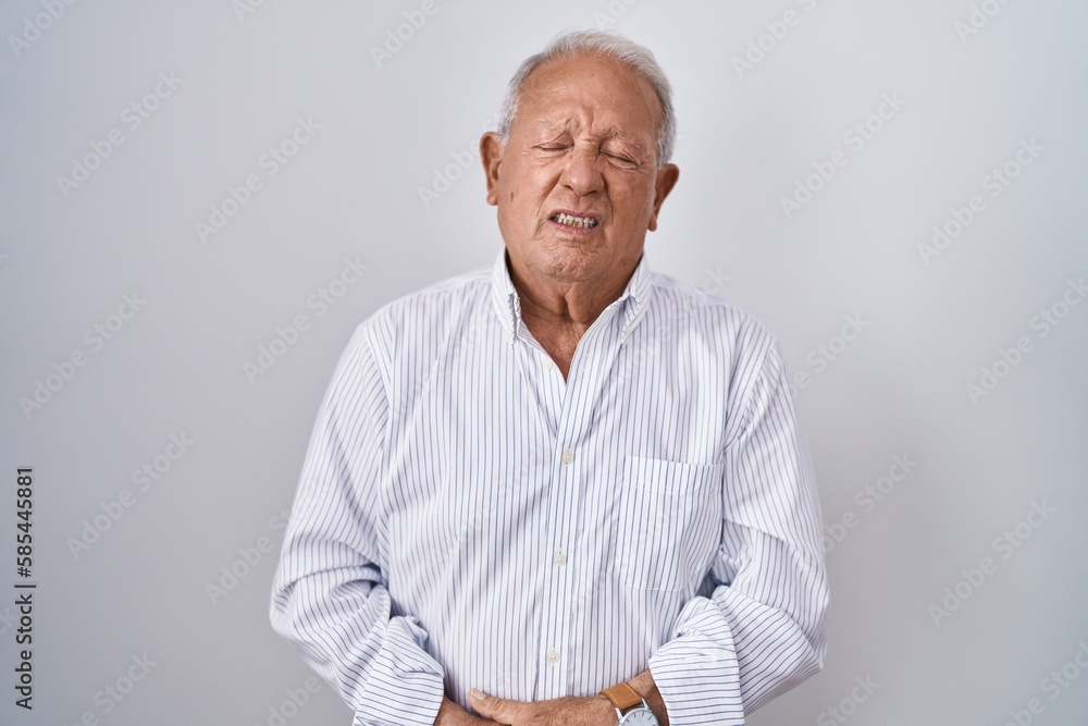 Senior man with grey hair standing over isolated background with hand on stomach because indigestion, painful illness feeling unwell. ache concept. Senior man with grey hair standing over isolated background with hand on stomach because indigestion, painful illness feeling unwell. ache concept.