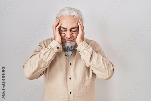 Middle age man with grey hair standing over isolated background with hand on head for pain in head because stress. suffering migraine.