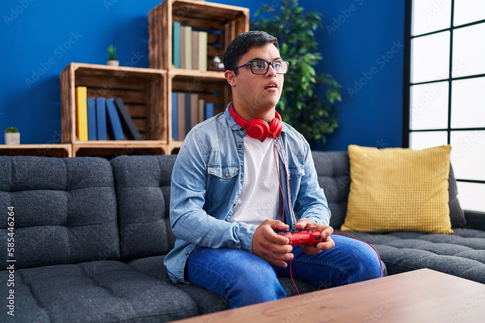 Down syndrome man playing video game sitting on sofa at home Down syndrome man playing video game sitting on sofa at home