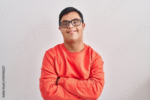 Young hispanic man with down syndrome standing over white background happy face smiling with crossed arms looking at the camera. positive person. photo