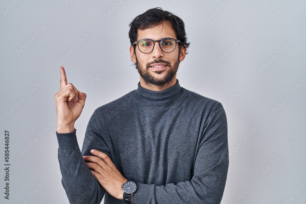 Handsome latin man standing over isolated background with a big smile on face, pointing with hand finger to the side looking at the camera. Handsome latin man standing over isolated background with a big smile on face, pointing with hand finger to the side looking at the camera.
