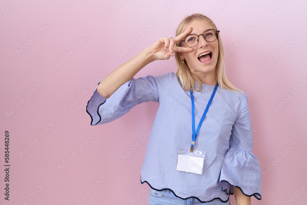 Young caucasian business woman wearing id card doing peace symbol with fingers over face, smiling cheerful showing victory Young caucasian business woman wearing id card doing peace symbol with fingers over face, smiling cheerful showing victory