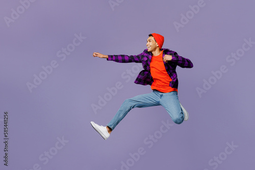 Fototapeta Naklejka Na Ścianę i Meble -  Full body side view young man of African American ethnicity wear casual shirt orange hat jump high with outstretched hands pov have super power isolated on plain pastel purple color background studio