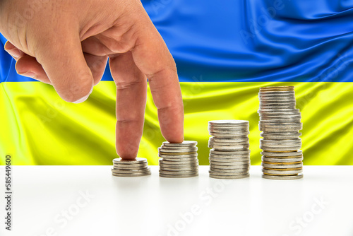 banknotes and coins in front of the national flag of Ukraine stack of silver and gold coin and hand gestures are walking for business concept. photo