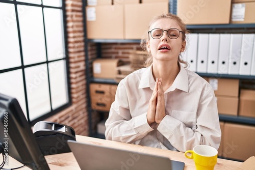 Fotografie Young caucasian woman working at small business ecommerce using laptop begging and praying with hands together with hope expression on face very emotional and worried
