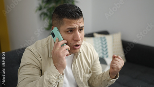 Young hispanic man speaking on the phone complaining at home photo
