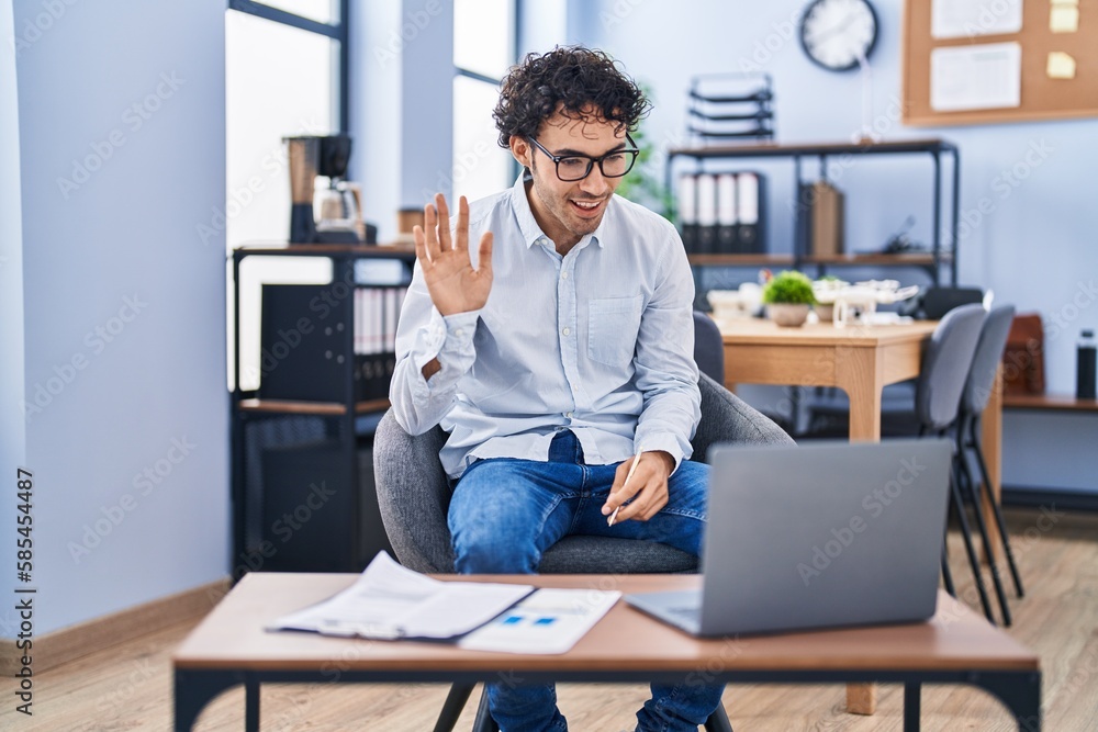 Hispanic man doing video call waving to laptop looking positive and happy standing and smiling with a confident smile showing teeth Hispanic man doing video call waving to laptop looking positive and happy standing and smiling with a confident smile showing teeth