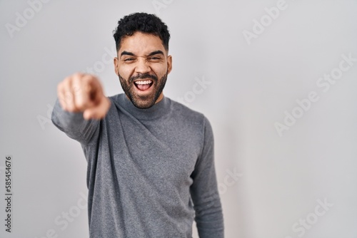 Hispanic man with beard standing over white background pointing displeased and frustrated to the camera, angry and furious with you