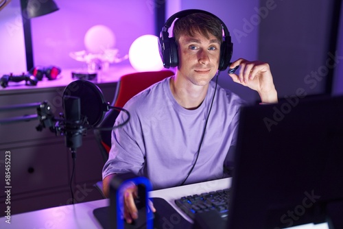 Young caucasian man streamer smiling confident sitting on table at gaming room