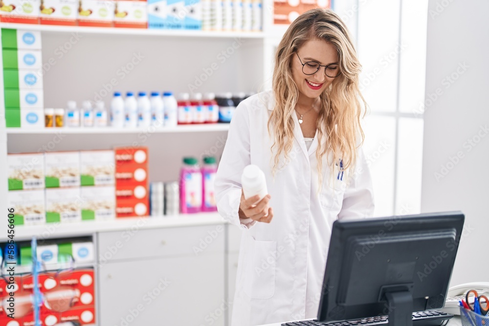 Young woman pharmacist holding pills bottle working at pharmacy