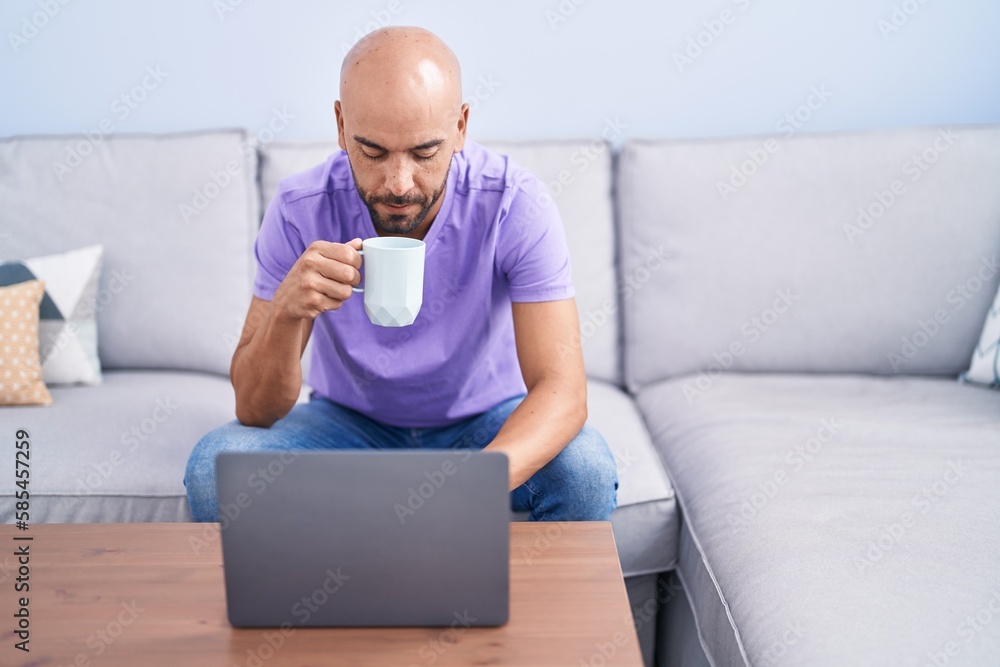 Young bald man using laptop drinking coffee at home Young bald man using laptop drinking coffee at home