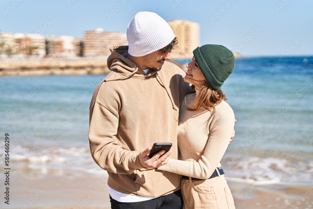 Mand and woman couple hugging each other using smartphone at seaside